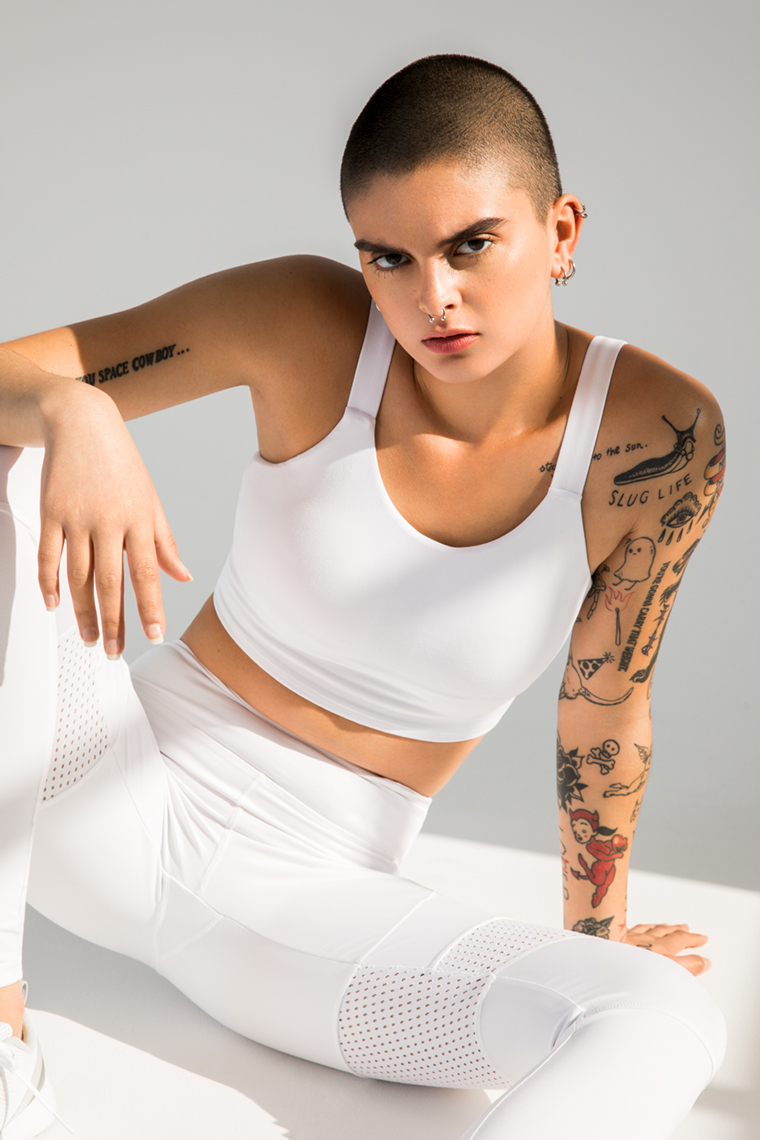 Portrait of woman with shaved head wearing white activewear sitting on floor of white studio