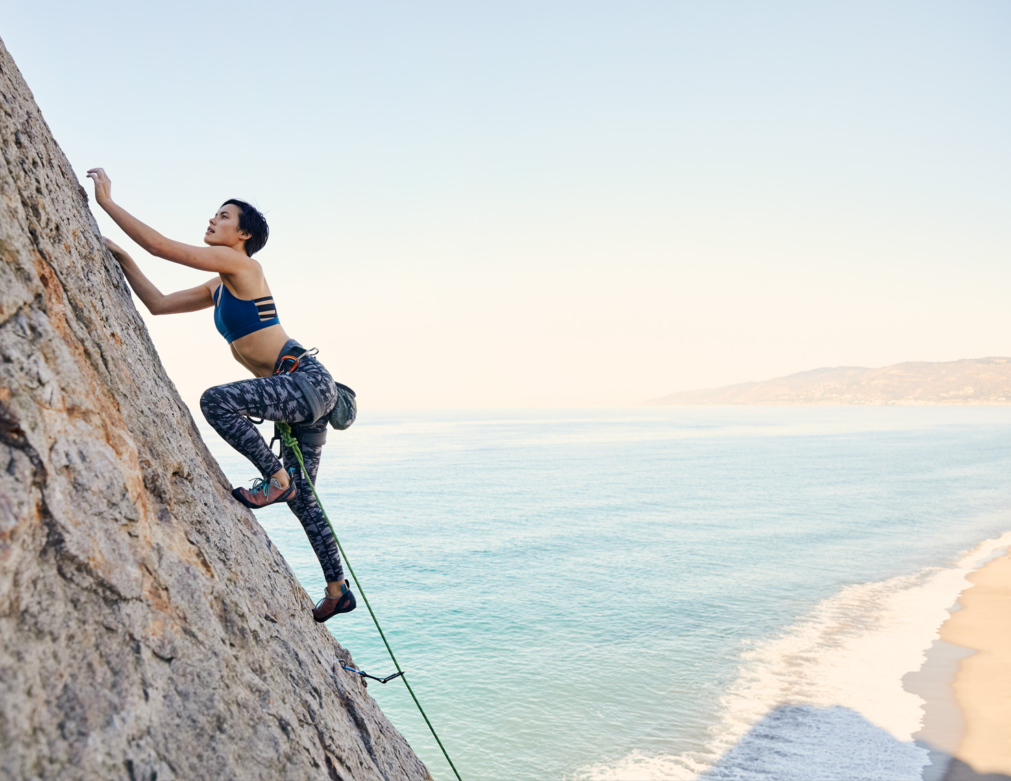 Woman rock climbing with the ocean behind her